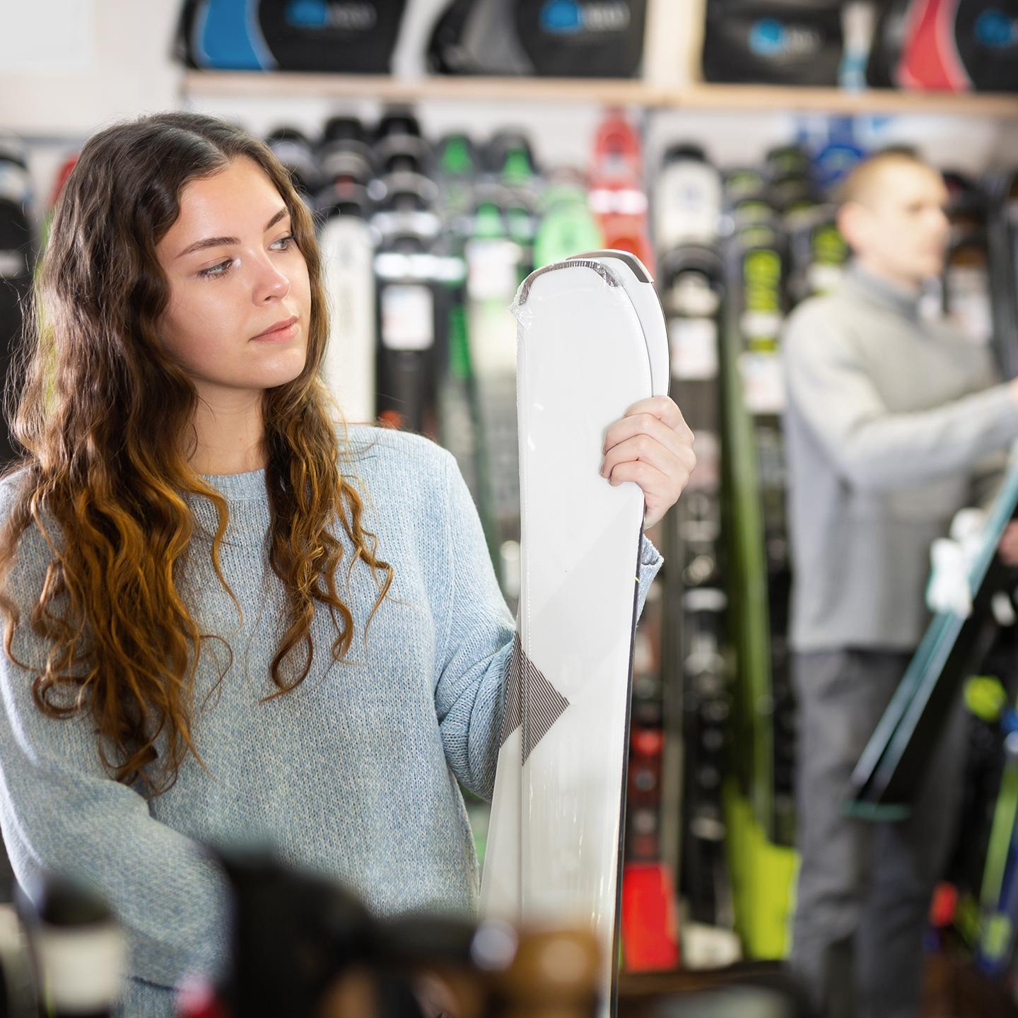 Une jeune femme est en train de choisir des skis dans un magasin de sport