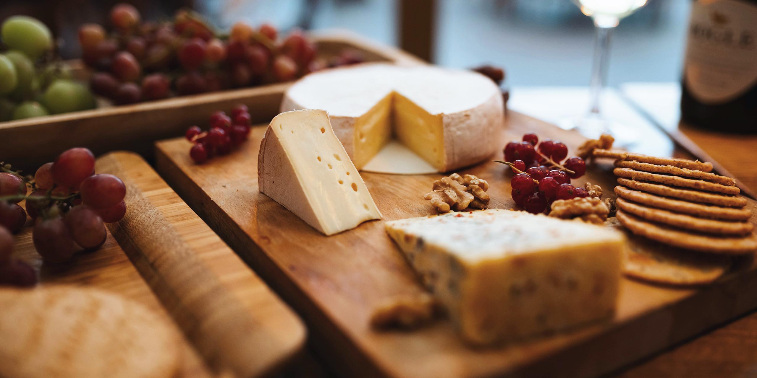 Plateau de fromages entouré de fruits et accompagné d'un verre de vin