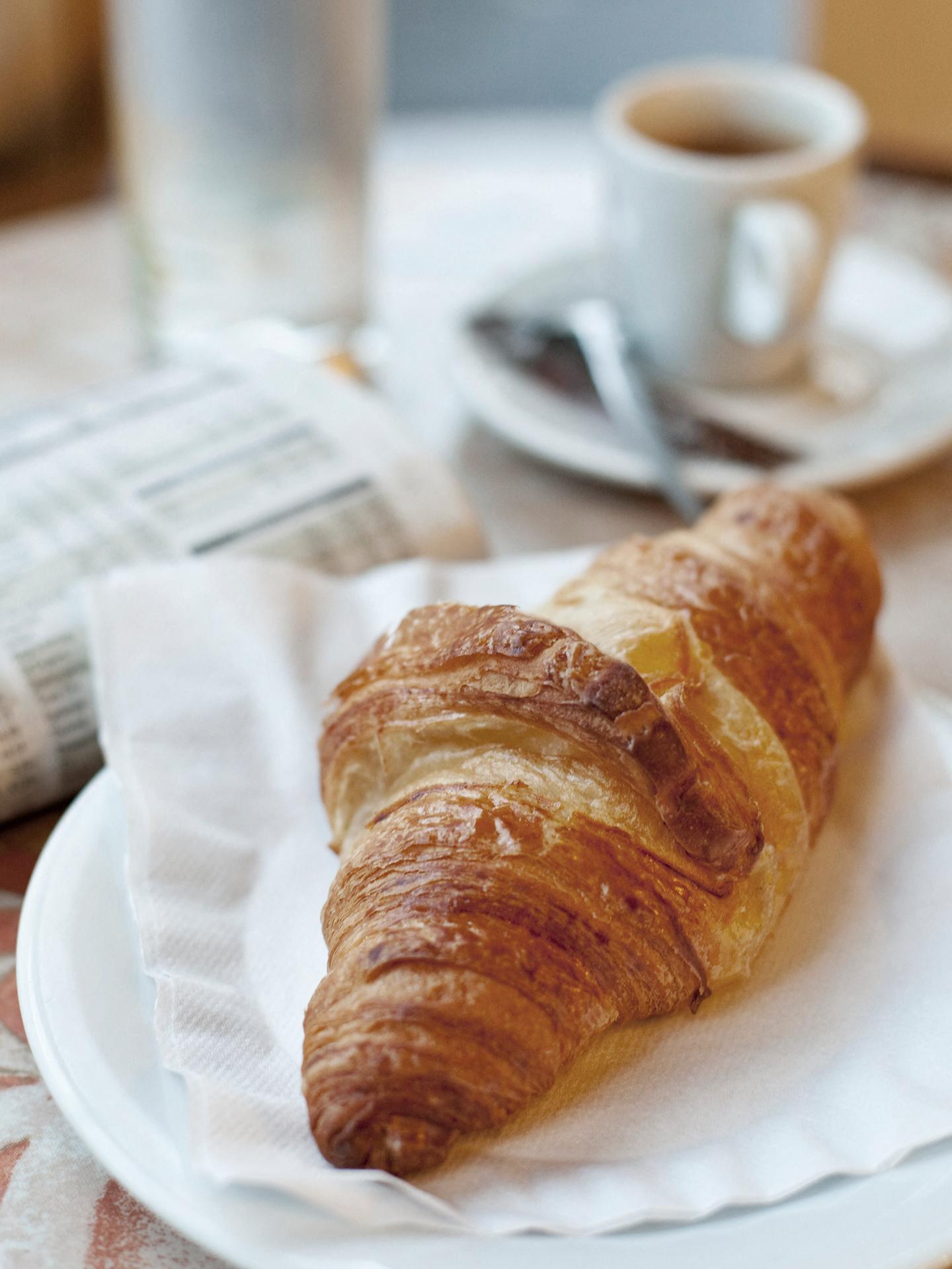 Un café et un croissant sont disposés sur une table avec un journal