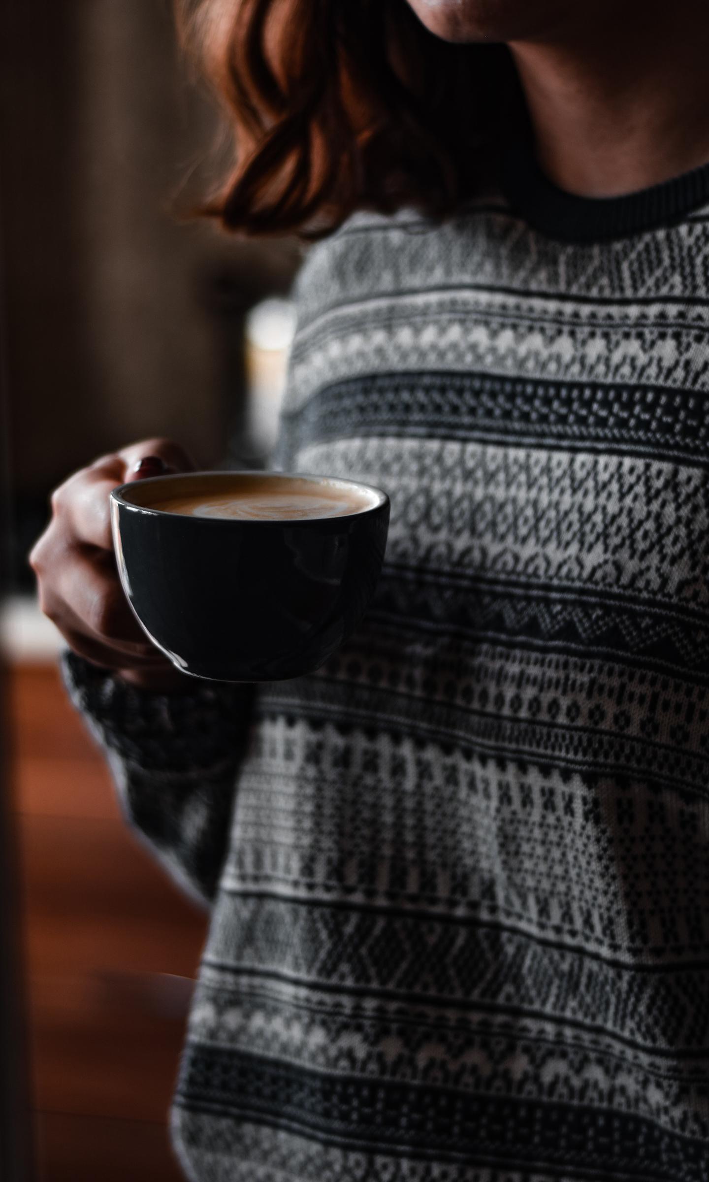 Une femme avec un pull Jacquard tient une tasse à café dans sa main