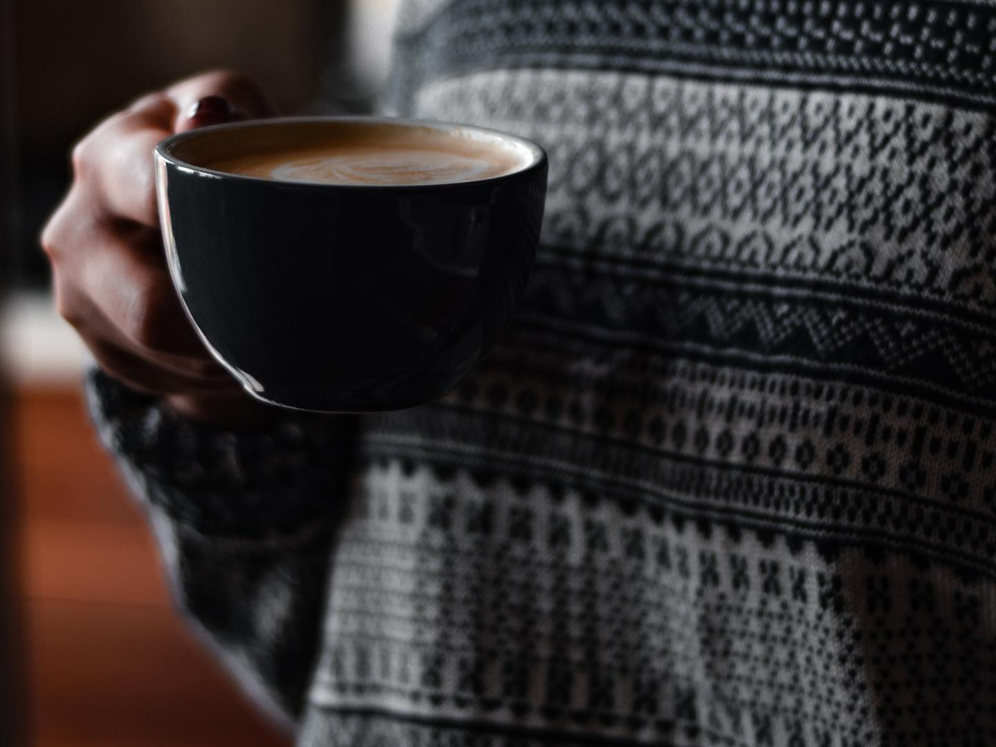 Une femme avec un pull Jacquard tient une tasse à café dans sa main