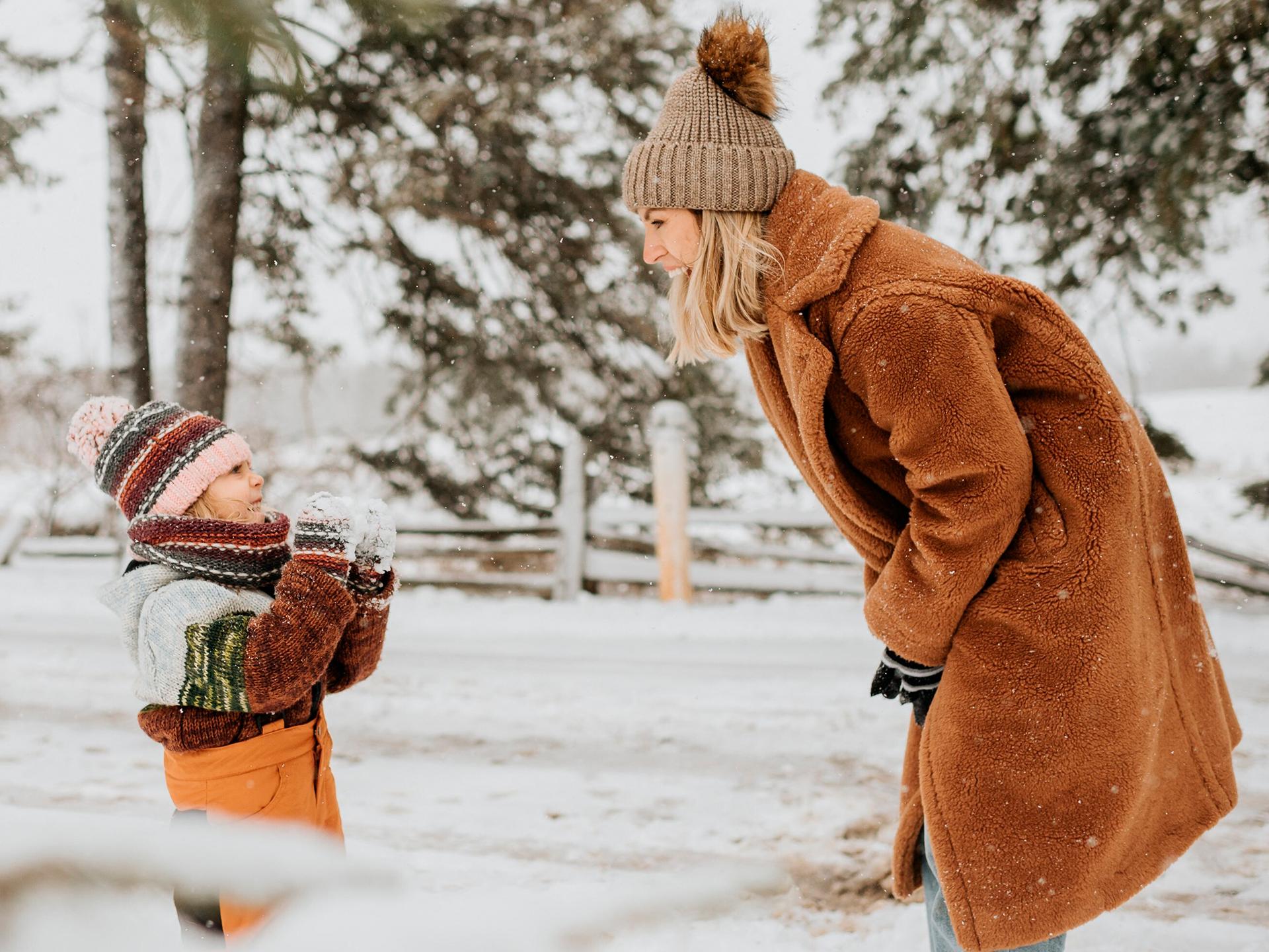 Un petit garçon joue et rigole avec sa maman dans la neige - Enfants et famille