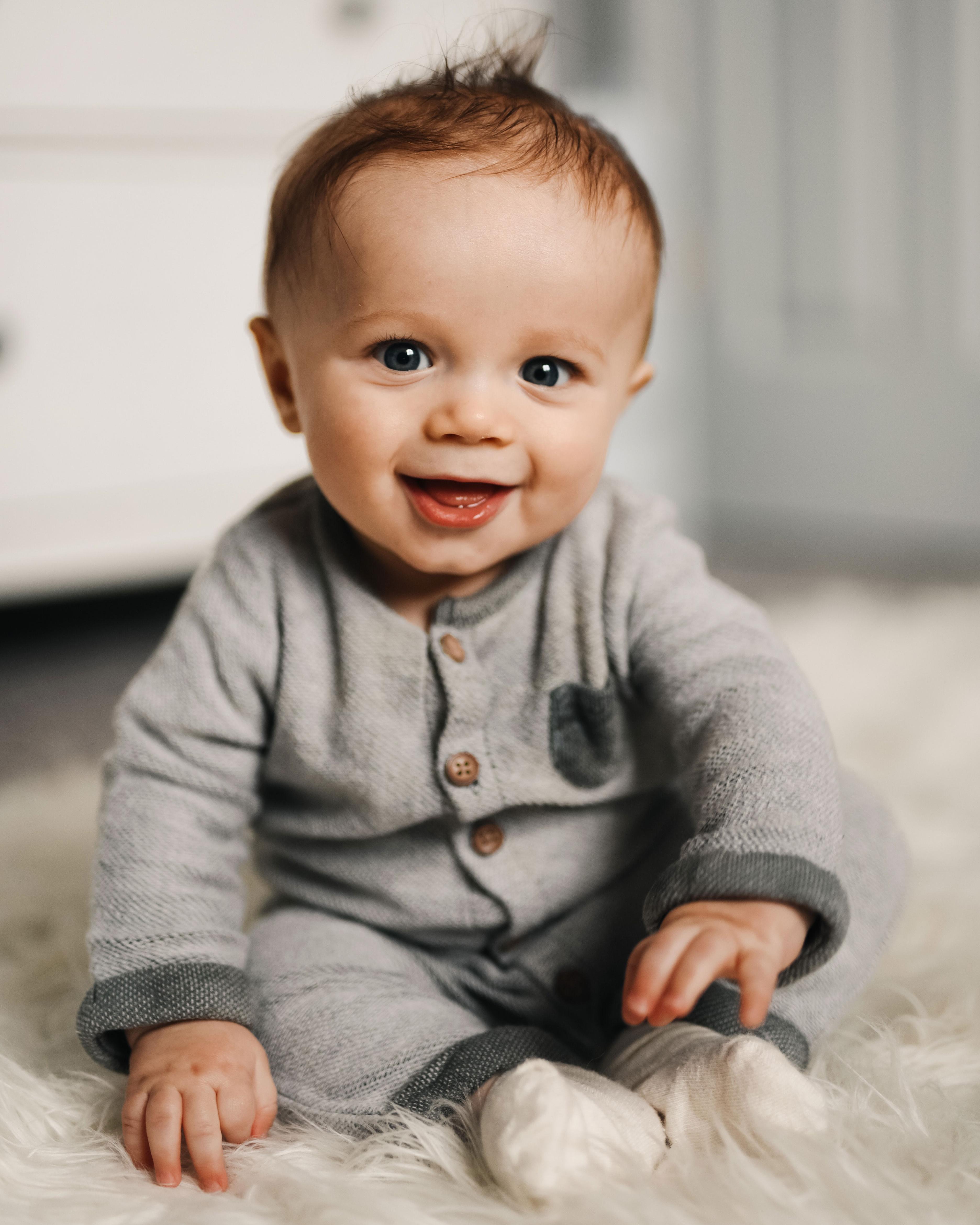 Un petit garçon souriant est assis sur un tapis 