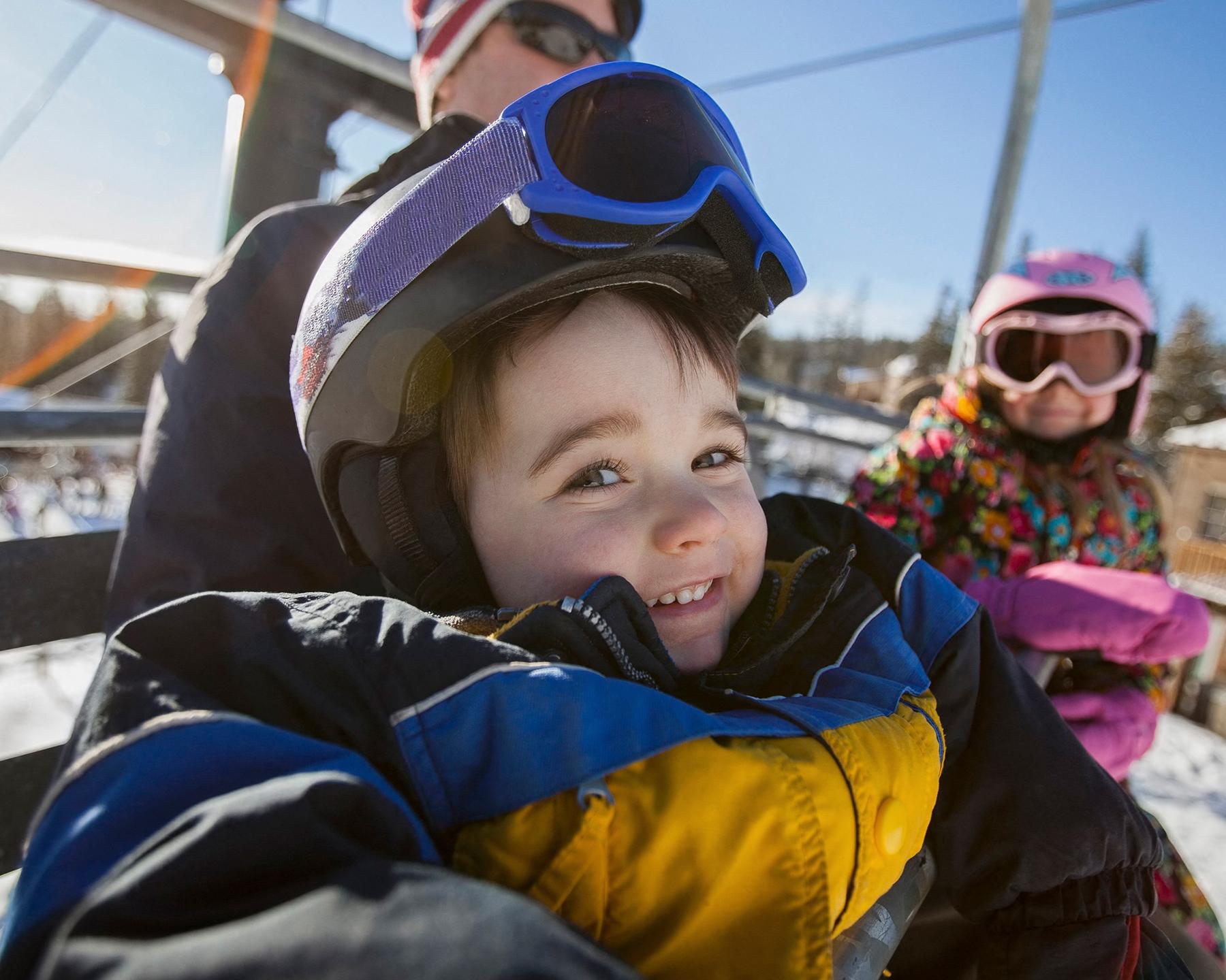 Un enfants est assis dans un télésiège emmitouflé dans sa combinaison de ski