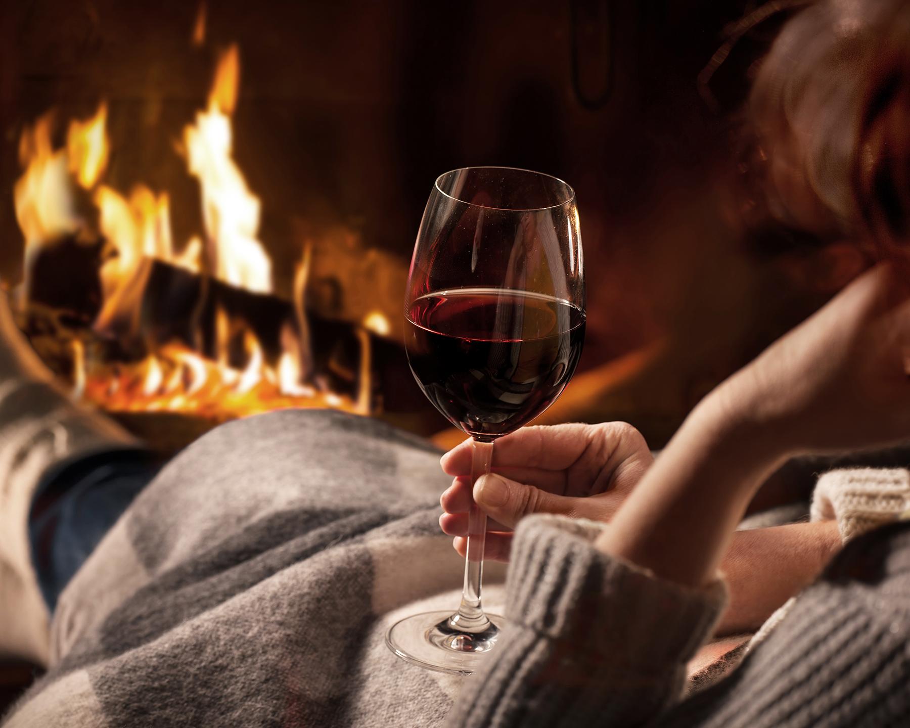 Une personne boit un verre de vin au coin de la cheminée
