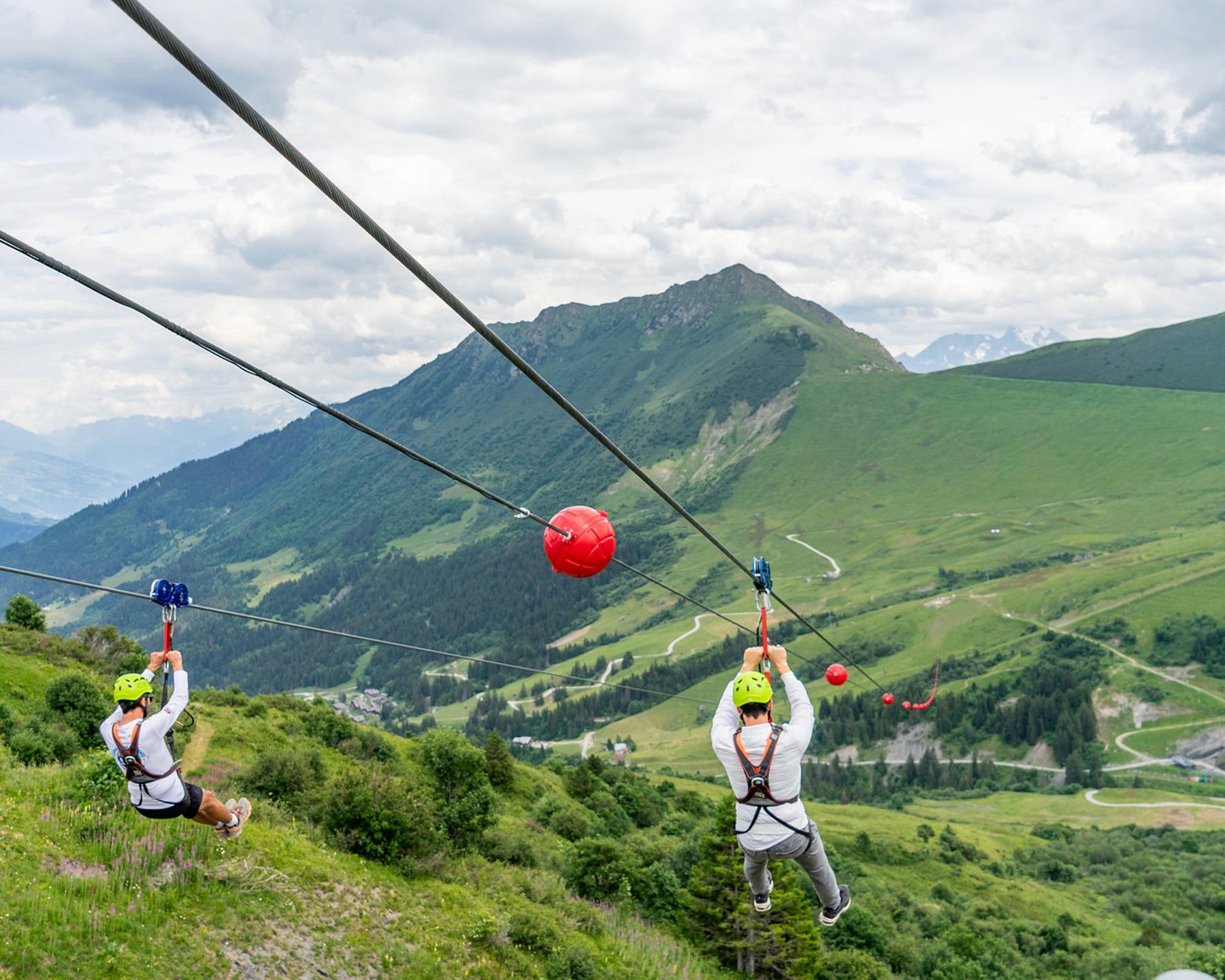 Deux hommes font de la tyrolienne à Valmorel, en été