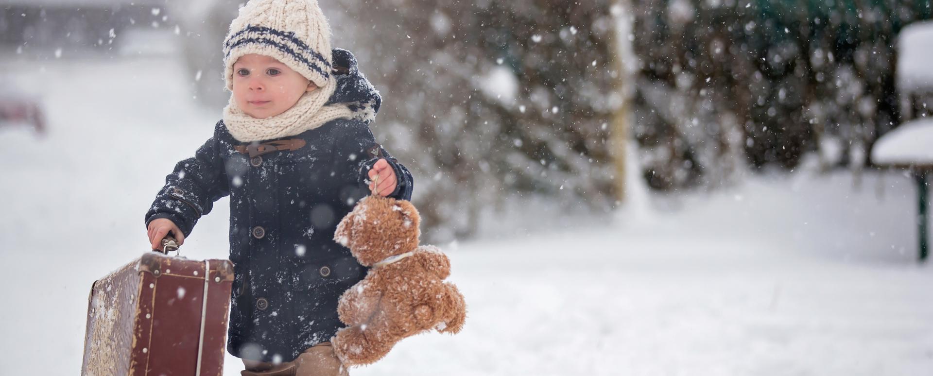 Petit garçon sous la neige transportant une valise