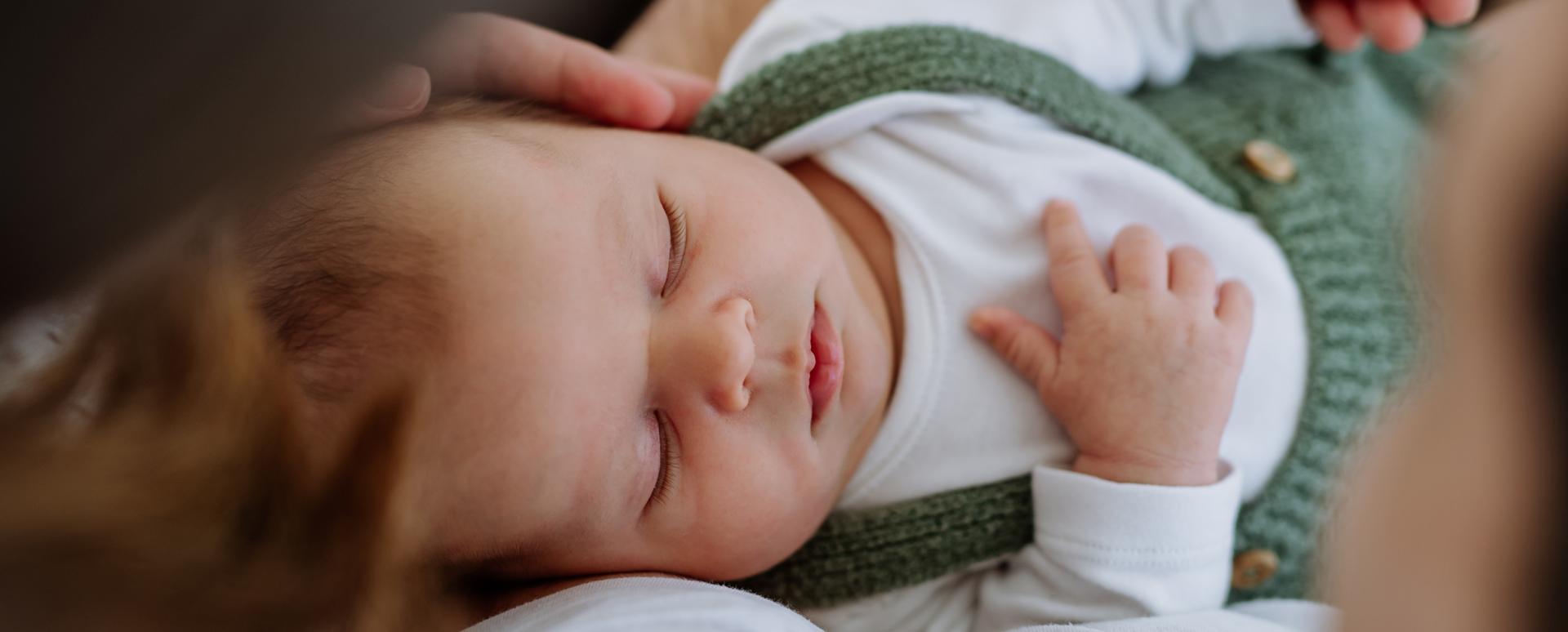 Un bébé dort dans les bras de sa maman